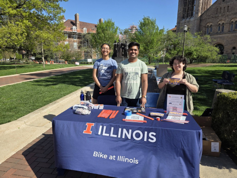 Two volunteers and Sarthak stand at a table with bike gear and swag