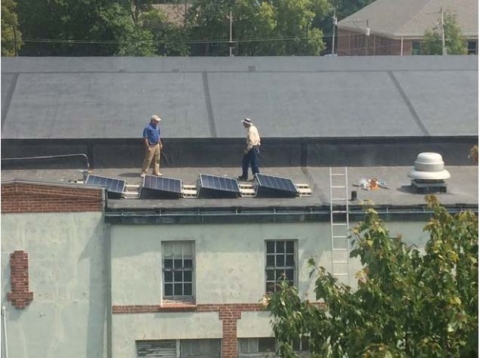 two men walk on a roof with four solar panels shown in the foreground