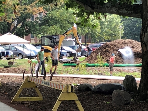 workers pass in front of tent, front loader, and large pile of mulch