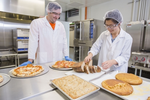 2 product development interns test & slice samples of bread made from project ingredients.