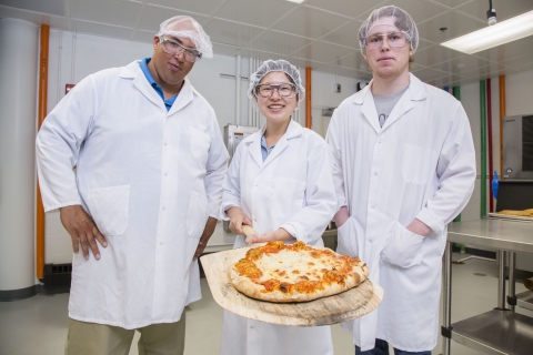 3 product development interns pose with the a cooked pizza using project ingredients.