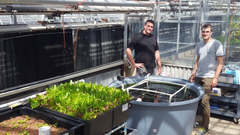 2 individuals posing next the aquaponics system; A zoomed-out perspective of the system