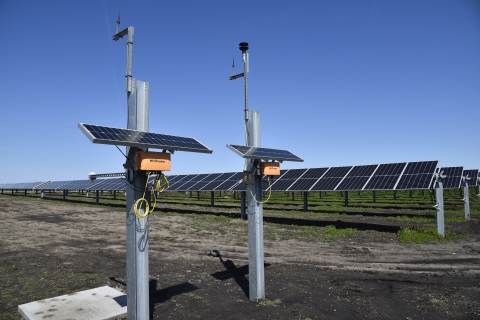 two poles with small solar panels hold orange NexTracker boxes in front of solar array rows