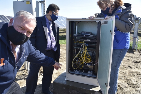 three people look at inside of networking box at solar farm
