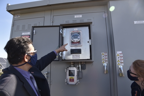 man points out open meter box on inverter to watching woman, both wearing masks