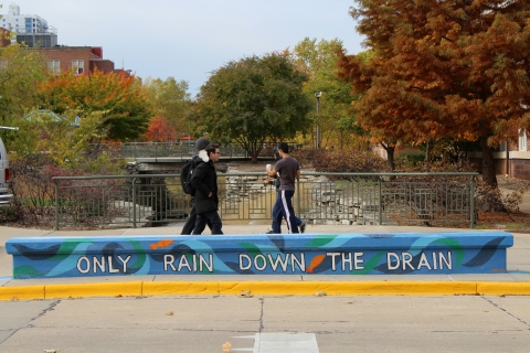A stone bench that says "Only Rain Down The Drain" with a painted ocean as the background