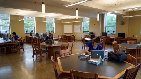 Students working in an open room with tables and computers.