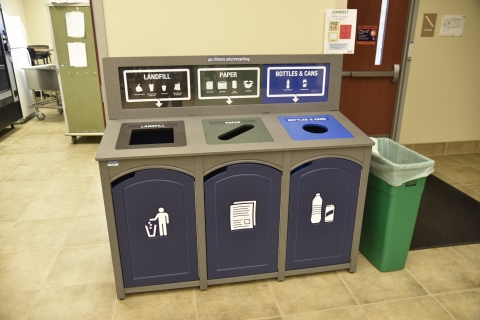 three bin recycling container with "landfill", "paper", and "bottles and cans" next to a temporary "compost" green container