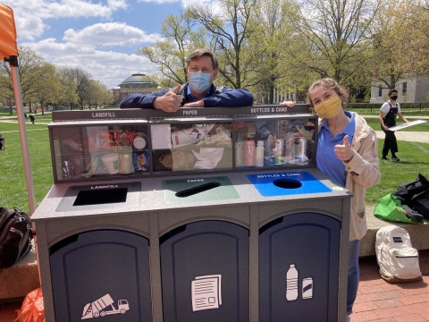 three part recycling bin with shadow boxes showing example recyclables, on Green Quad Day with David Guth and Maddy Liberman showing two thumbs up
