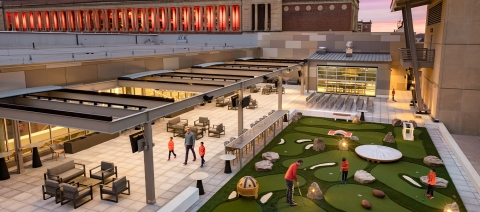 An outdoor patio on the roof of the building with lots of seating and mini golf.