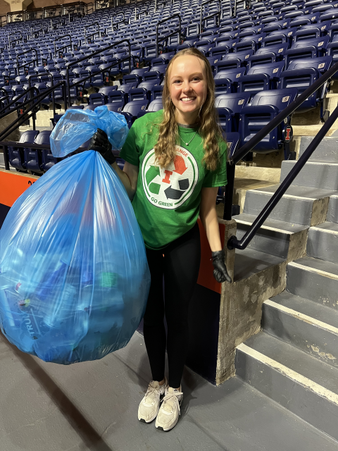 Volunteer collecting recyclables in a blue bag.